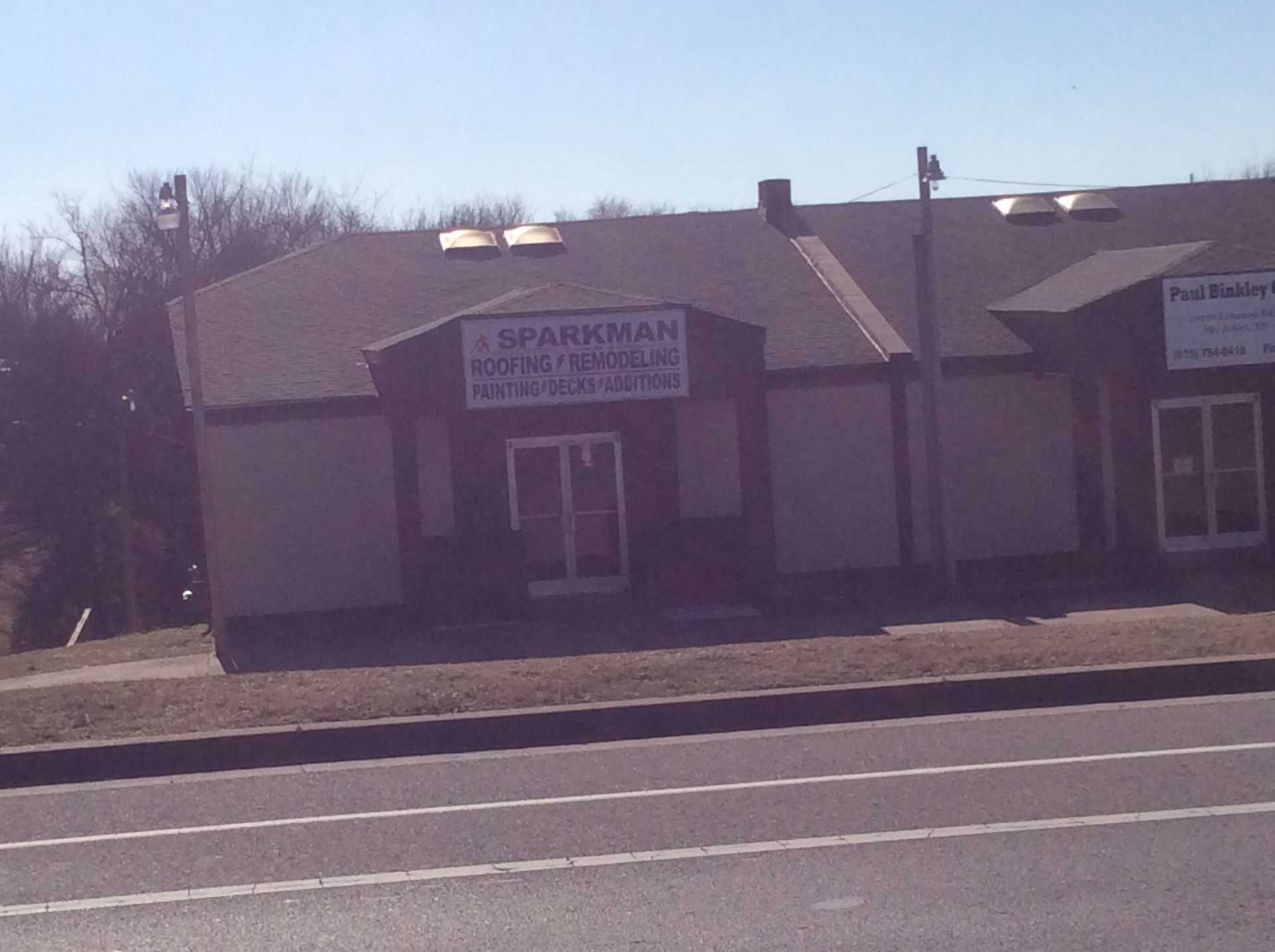 A single-story commercial building with tan siding and a dark shingled roof, featuring a sign reading 