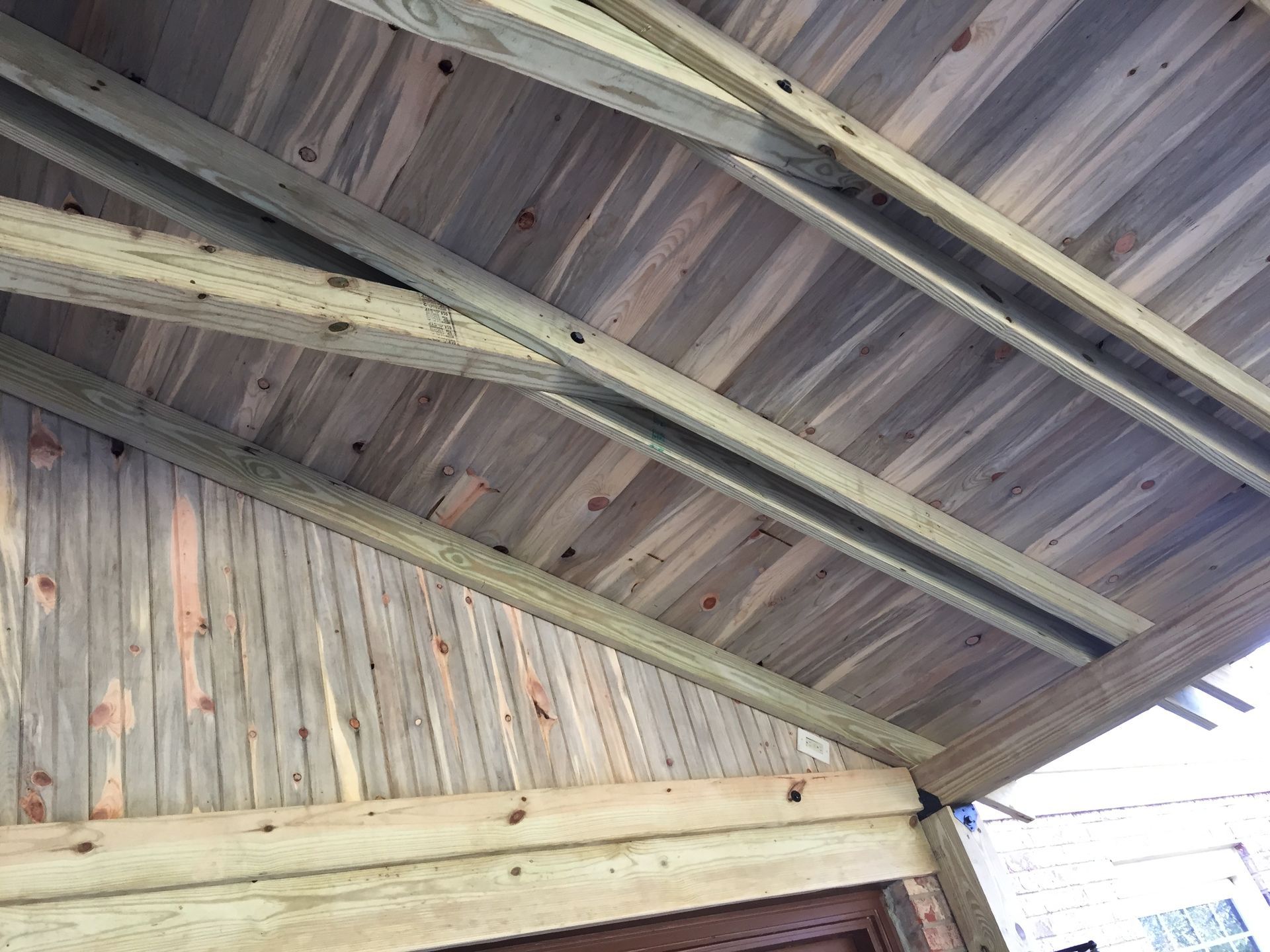 A low-angle view of a wooden ceiling structure with angled beams and rustic, vertical wood-paneled walls.