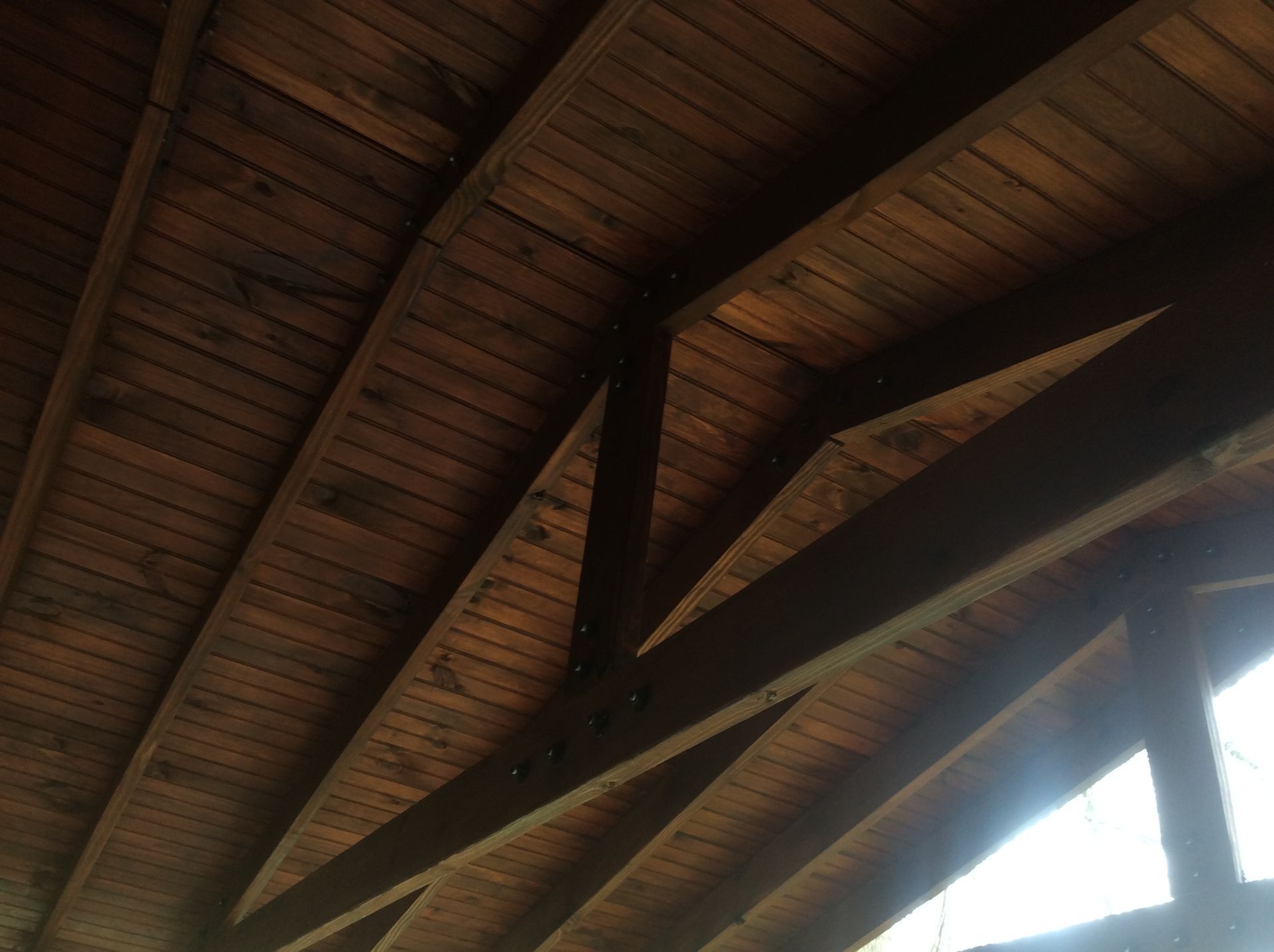 A low-angle view of a wooden ceiling featuring exposed support beams, rafters, and planking.