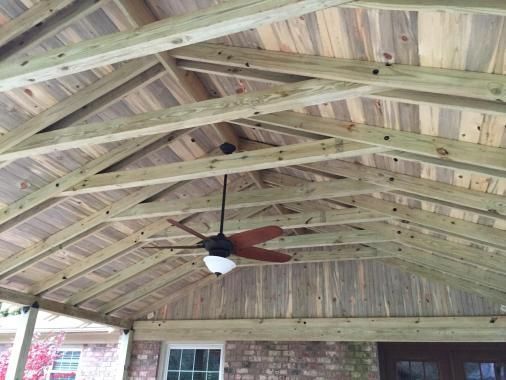 Ceiling view of a covered patio with exposed wooden rafters, pine ceiling planks, and a ceiling fan.