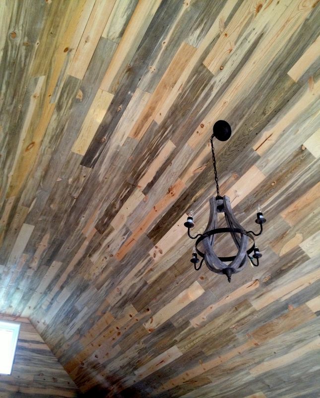 A rustic ceiling made of varying tones of reclaimed wood planks, featuring a hanging black metal chandelier.