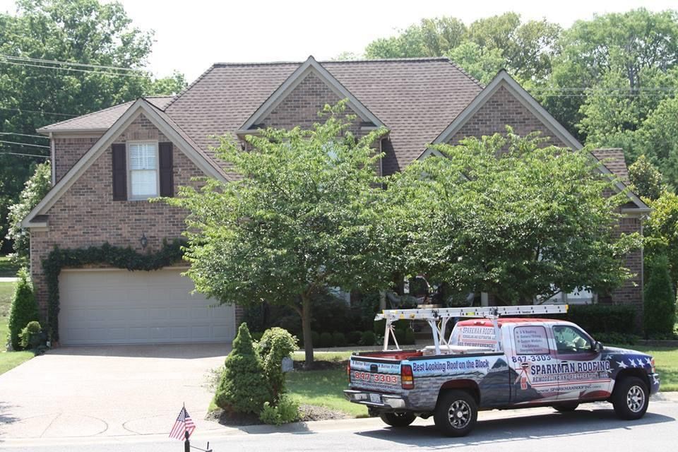 A two-story brick house with a two-car garage and a service truck parked in the driveway.