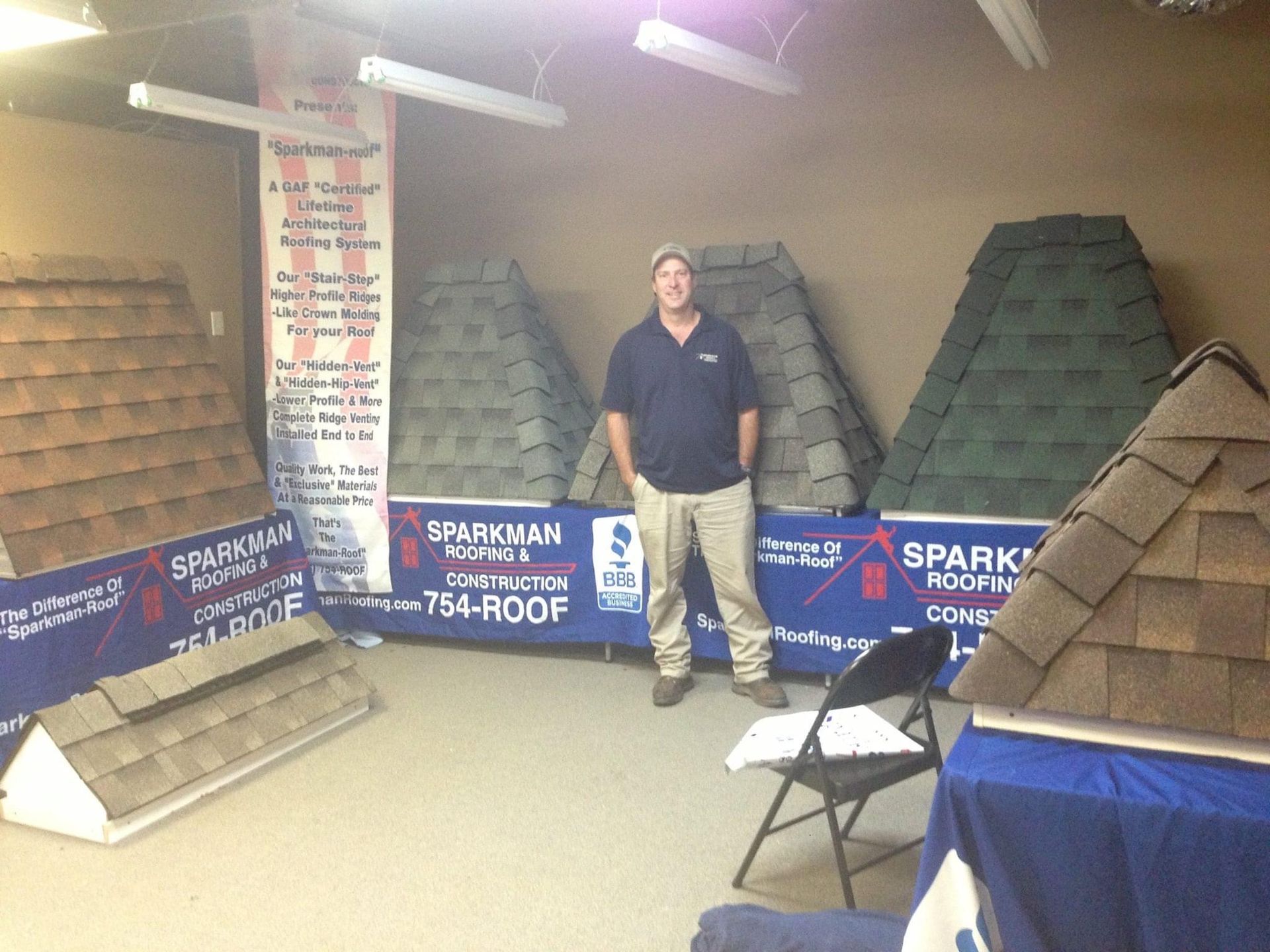 A man stands in a showroom featuring various rooftop shingle samples for Sparkman Roofing.
