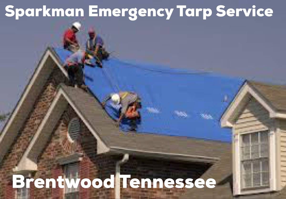 Workers in hard hats secure a large blue emergency tarp over the roof of a house in Brentwood, Tennessee.