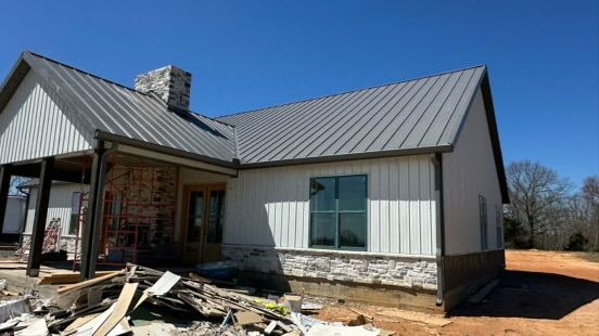 A modern house with white vertical siding, a grey metal roof, and a stone facade, under a clear blue sky.