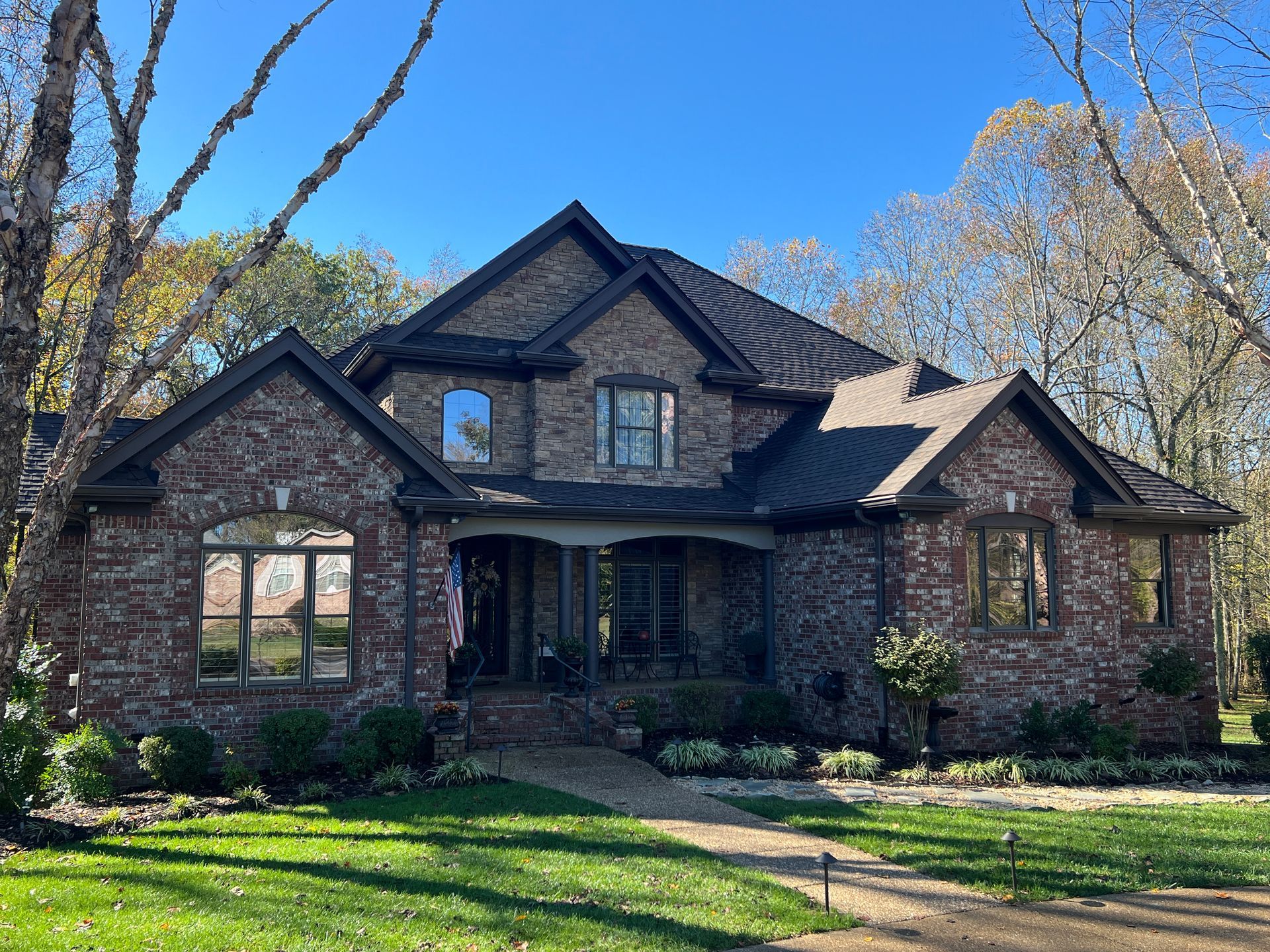 Two-story brick house with a dark roof and a walkway leading to the front porch on a sunny day.