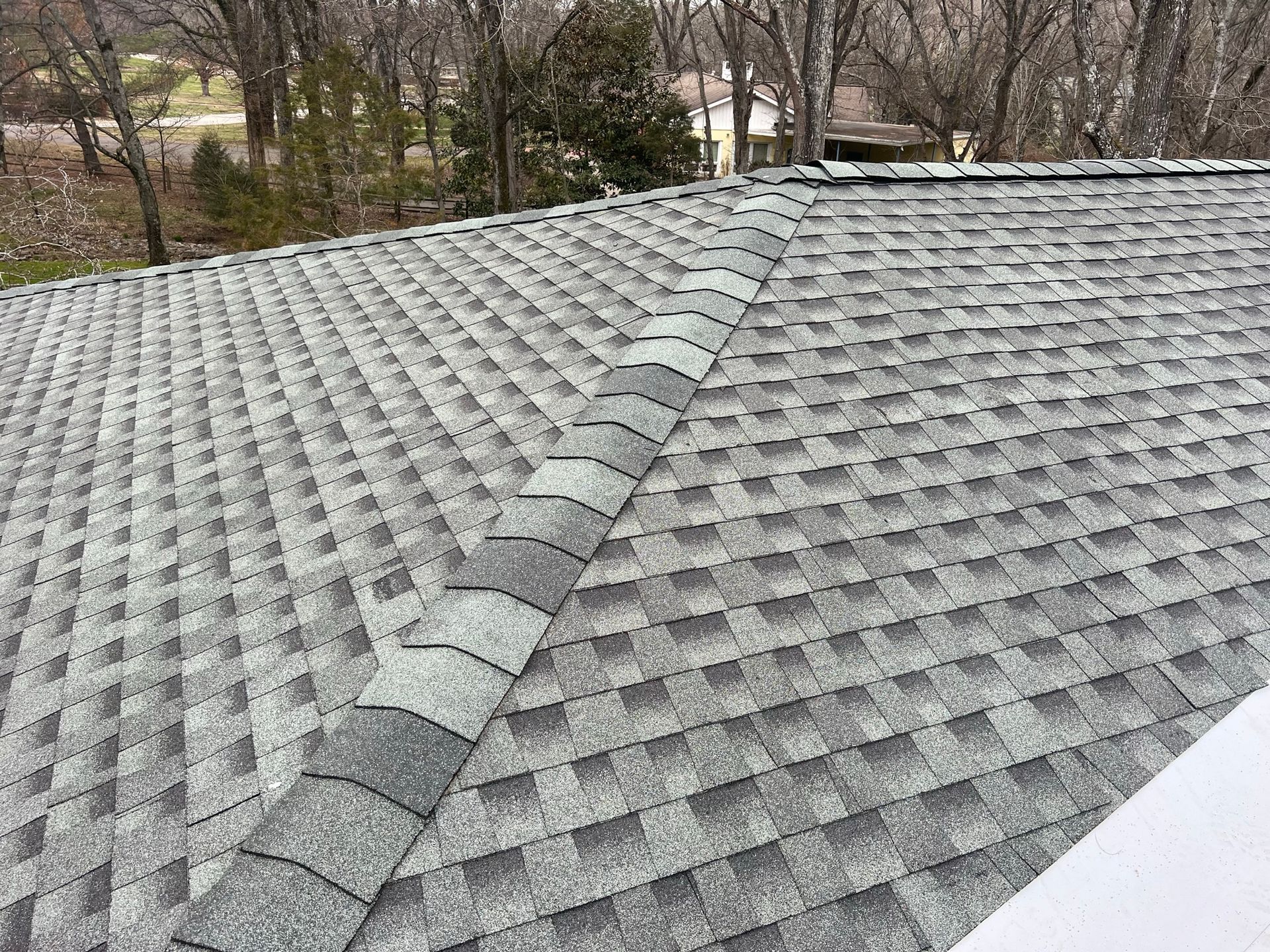 A close-up of a residential roof featuring gray asphalt architectural shingles and a matching ridge cap.