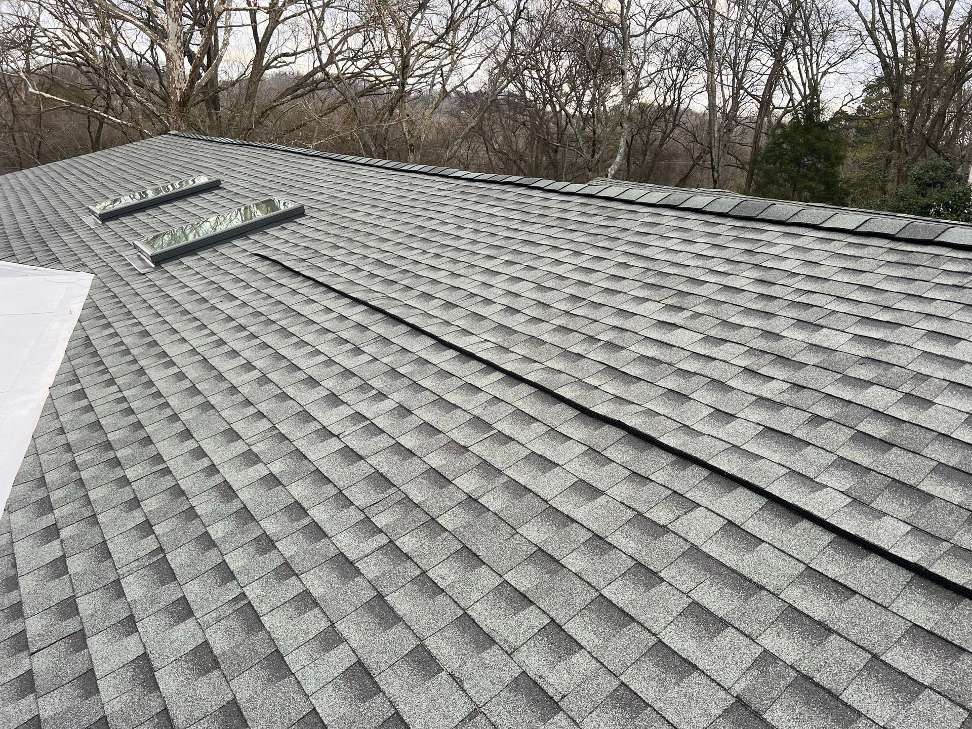 A residential roof with grey asphalt shingles, featuring two skylights and a long, horizontal ridge vent.