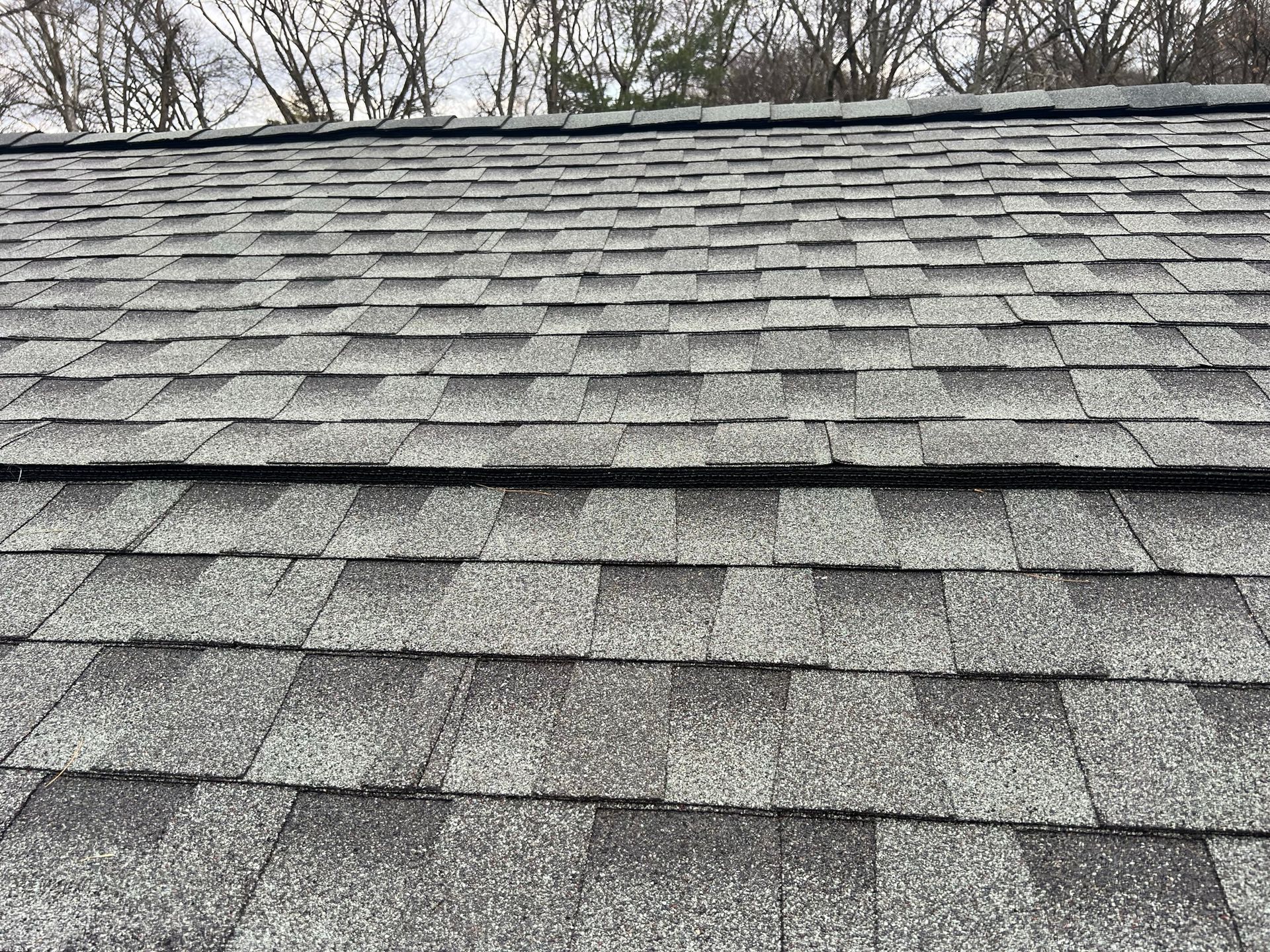 Close-up of a weathered, grey asphalt shingle roof with a horizontal ridge cap visible at the top.