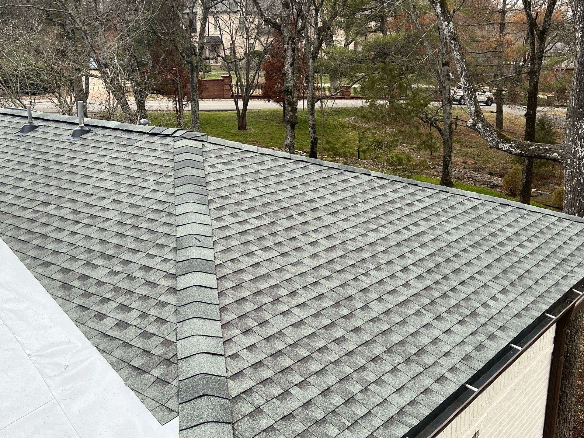 A high-angle view of a grey shingled roof with a central ridge line, partially covered by white protective underlayment.