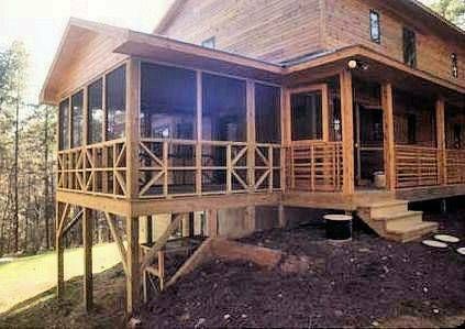 A wooden cabin exterior featuring a screened-in porch with lattice railing on a sloped, mulched landscape.
