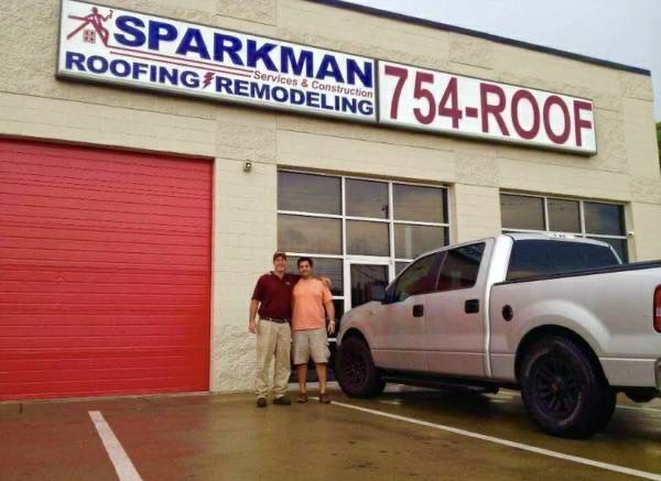 Two people standing outside a Sparkman Roofing & Remodeling building next to a pickup truck.