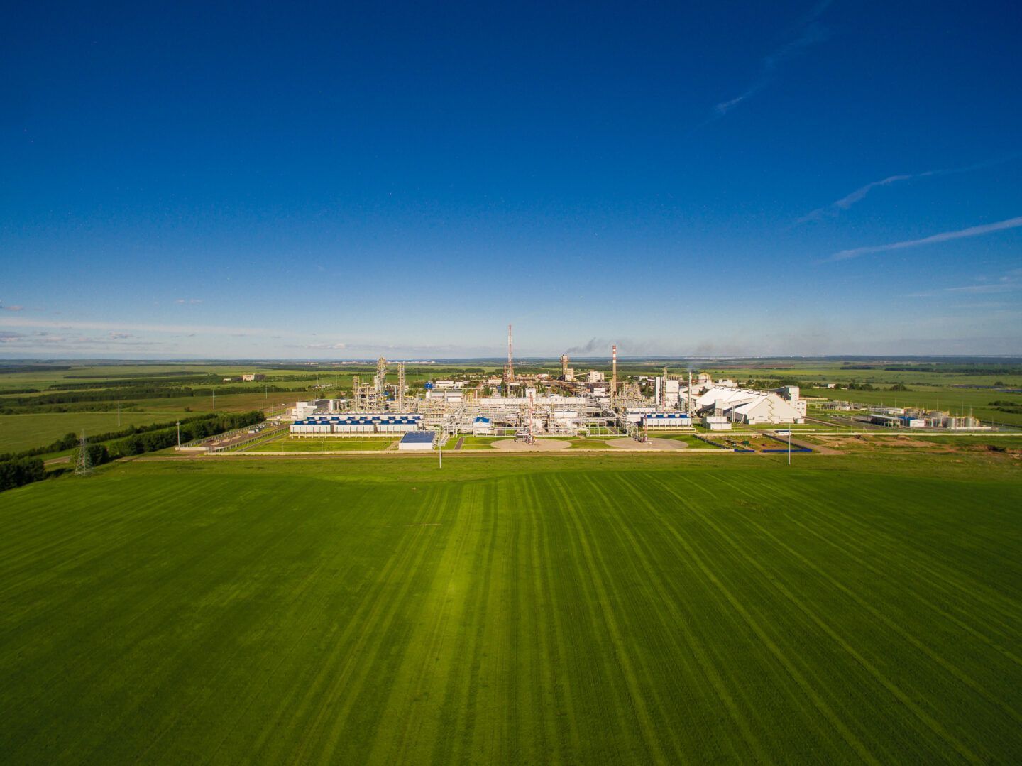 Factory complex in a green field under a blue sky.