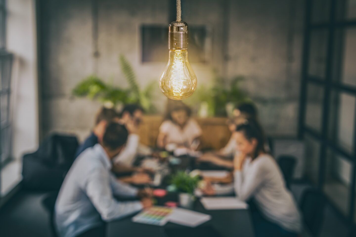 Bright lightbulb above a blurred group of people at a meeting.