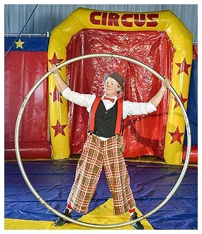 A clown is holding a hula hoop in front of a circus tent