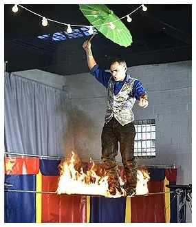 A man is standing on a tightrope holding an umbrella over a fire