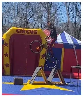A man is doing a trick on a bike in front of an inflatable circus tent.