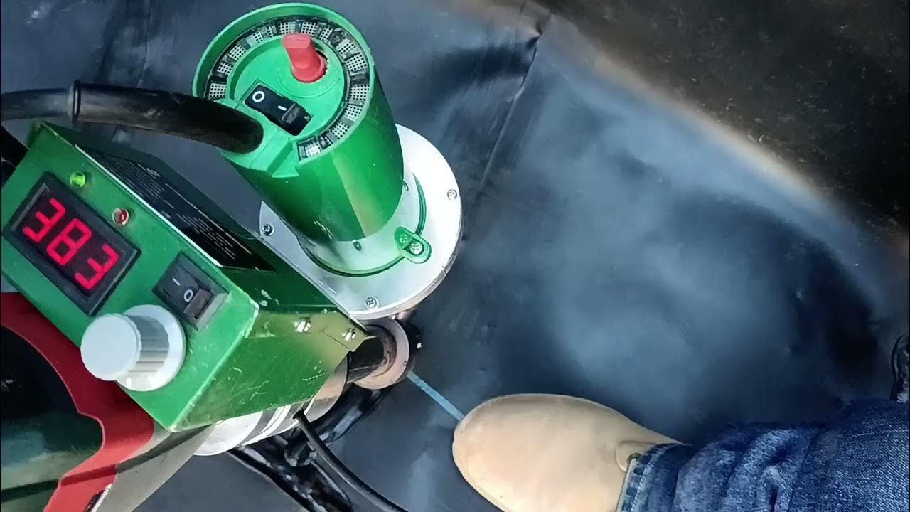 Green welding tool sealing black plastic with a digital temperature display. A person's boot is in view.