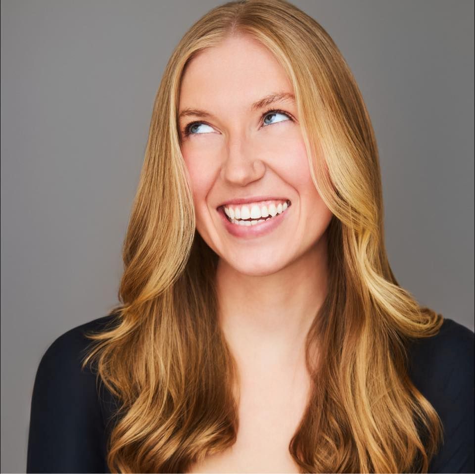 Blonde woman smiles, looking up and to the left against a gray backdrop.