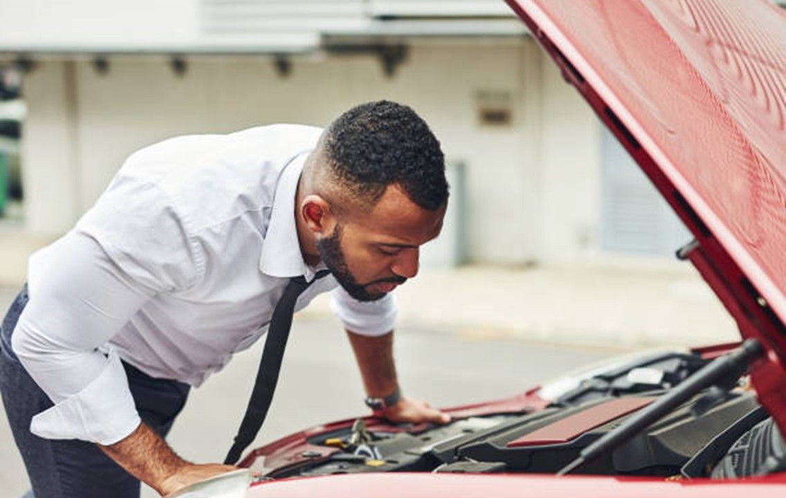 A Man Is Looking Under the Hood of A Car at Sunset.