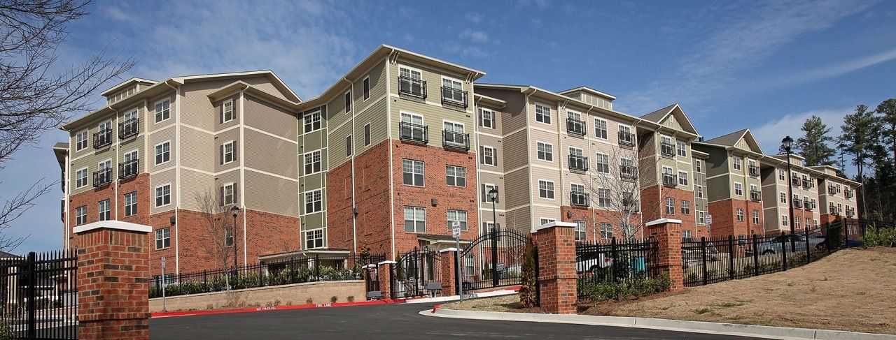 Exterior view of a multi-story apartment community with brick and beige siding and a gated entrance.