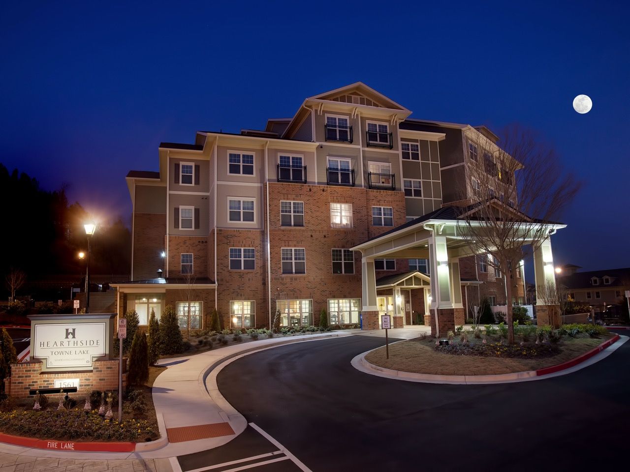 Exterior view of a multi-story apartment building at night with a curved driveway and lit entrance.