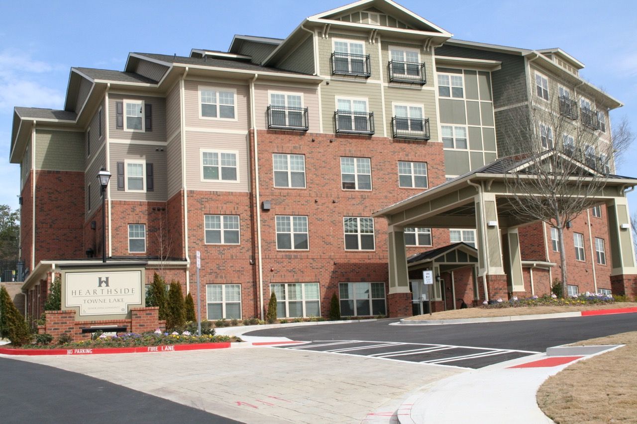 Exterior view of a modern apartment building with brick facade, covered entrance, and landscaped surroundings.