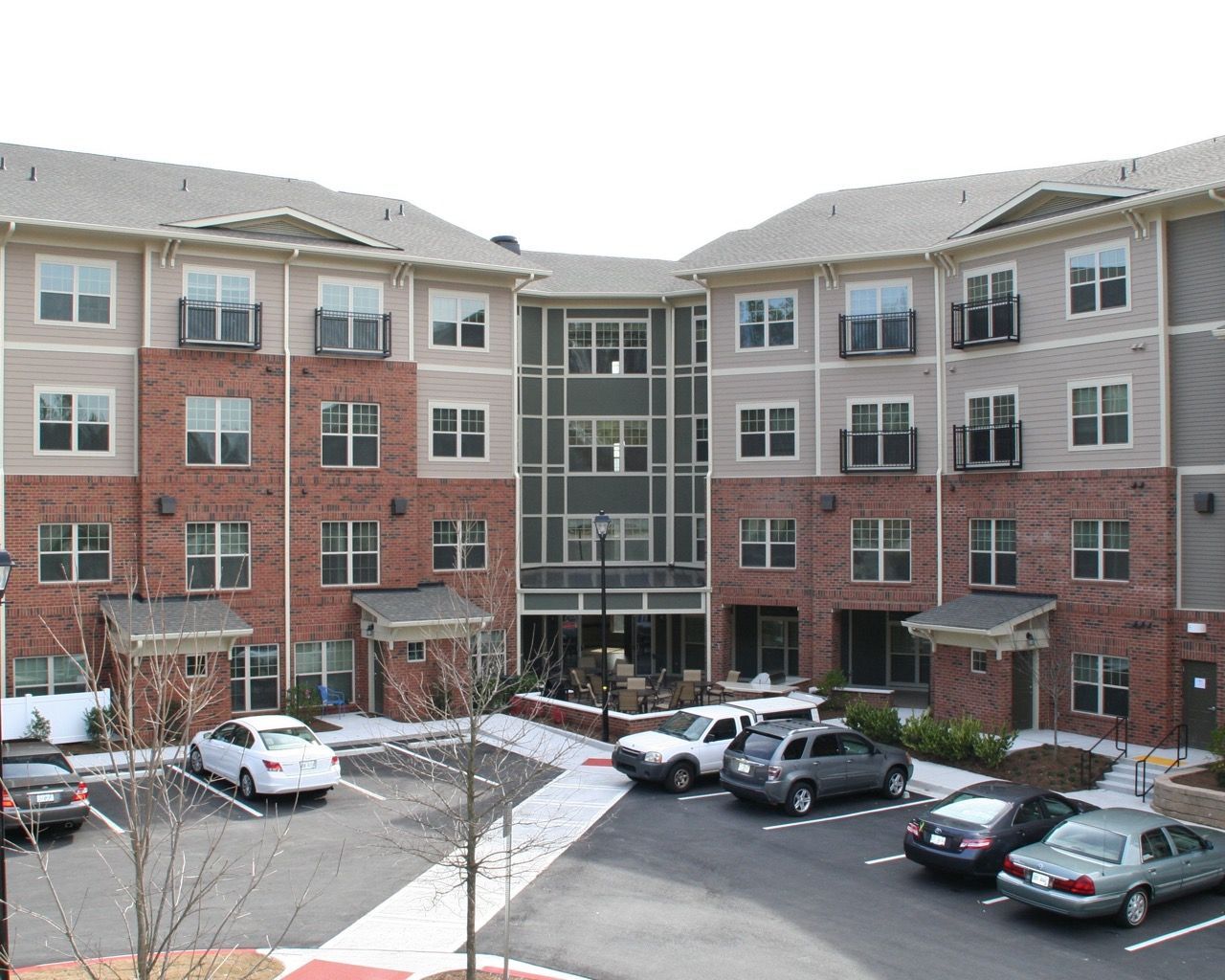 Exterior view of a modern apartment building with brick base, central glass atrium, and parking.