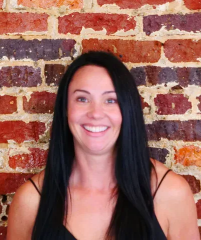 Doctor wearing glasses, stethoscope, and lab coat, holding clipboard, talking on screen.