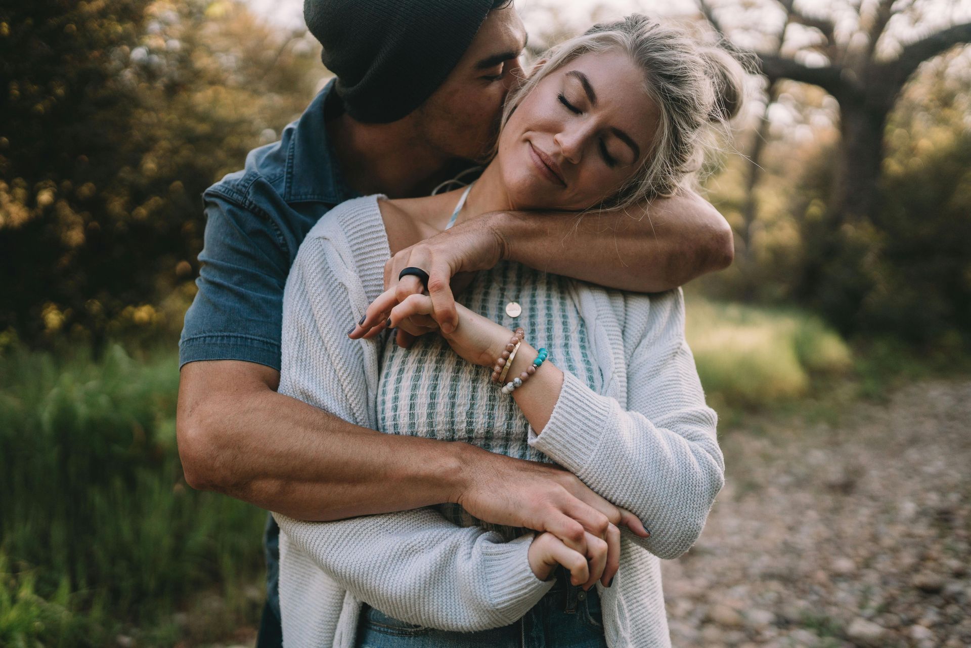 Man kissing woman's cheek outdoors; she smiles, arms wrapped around herself. Man kissing woman's cheek outdoors; she smiles, arms wrapped around herself.