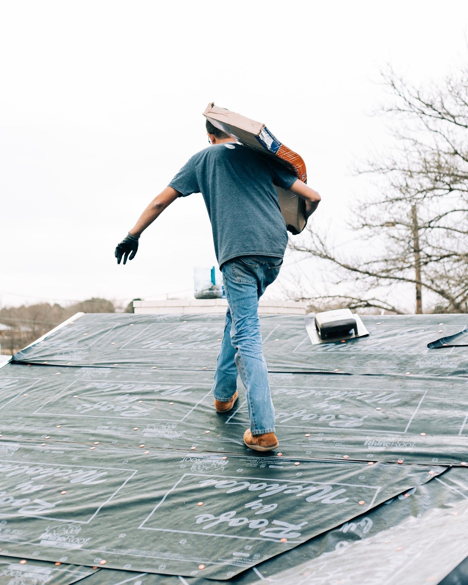 Roofer carrying bundle of shingles across prepared roof underlayment during installation