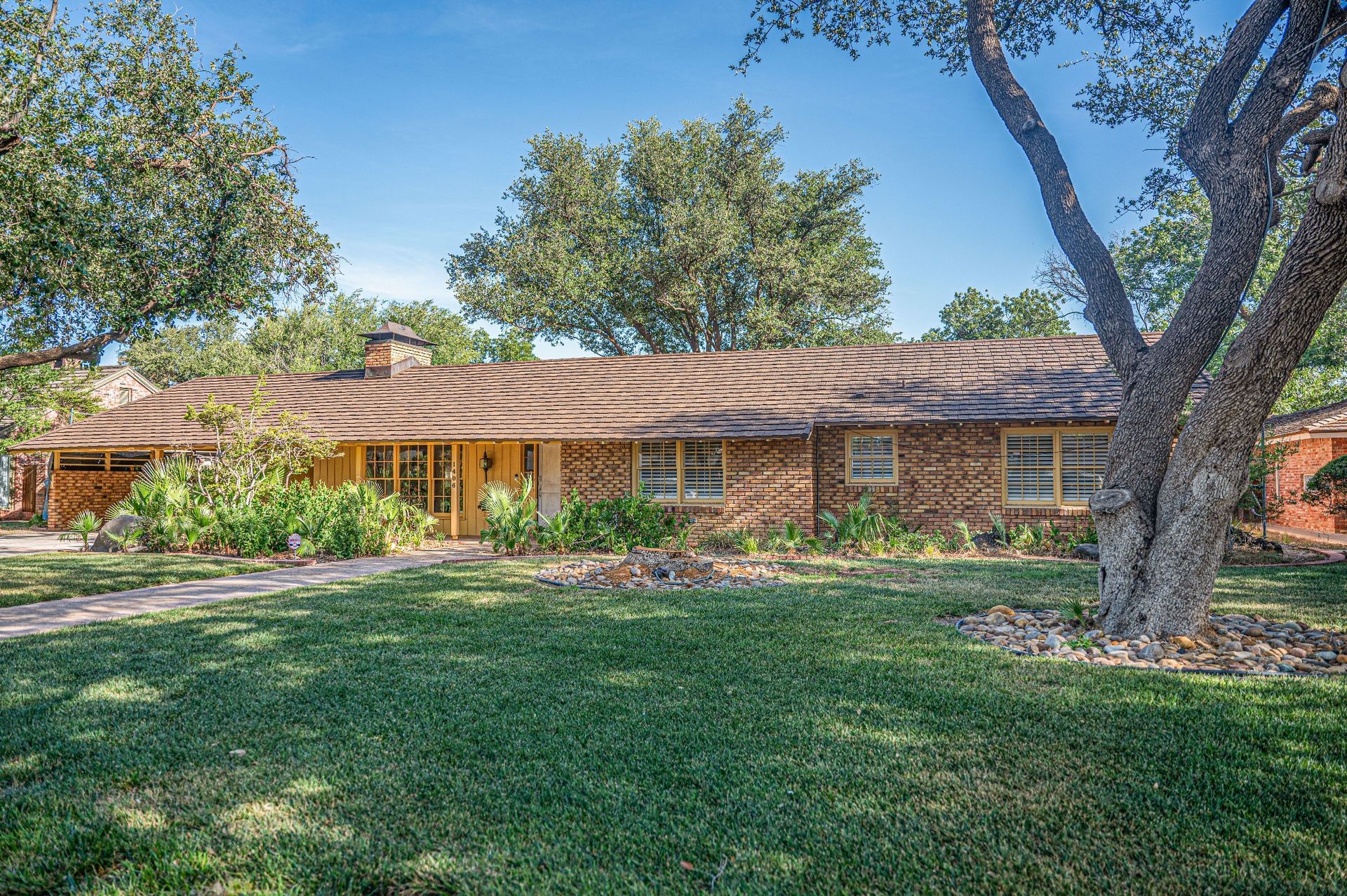 Front view of single-story brick home with brown shingle roof and landscaped yard