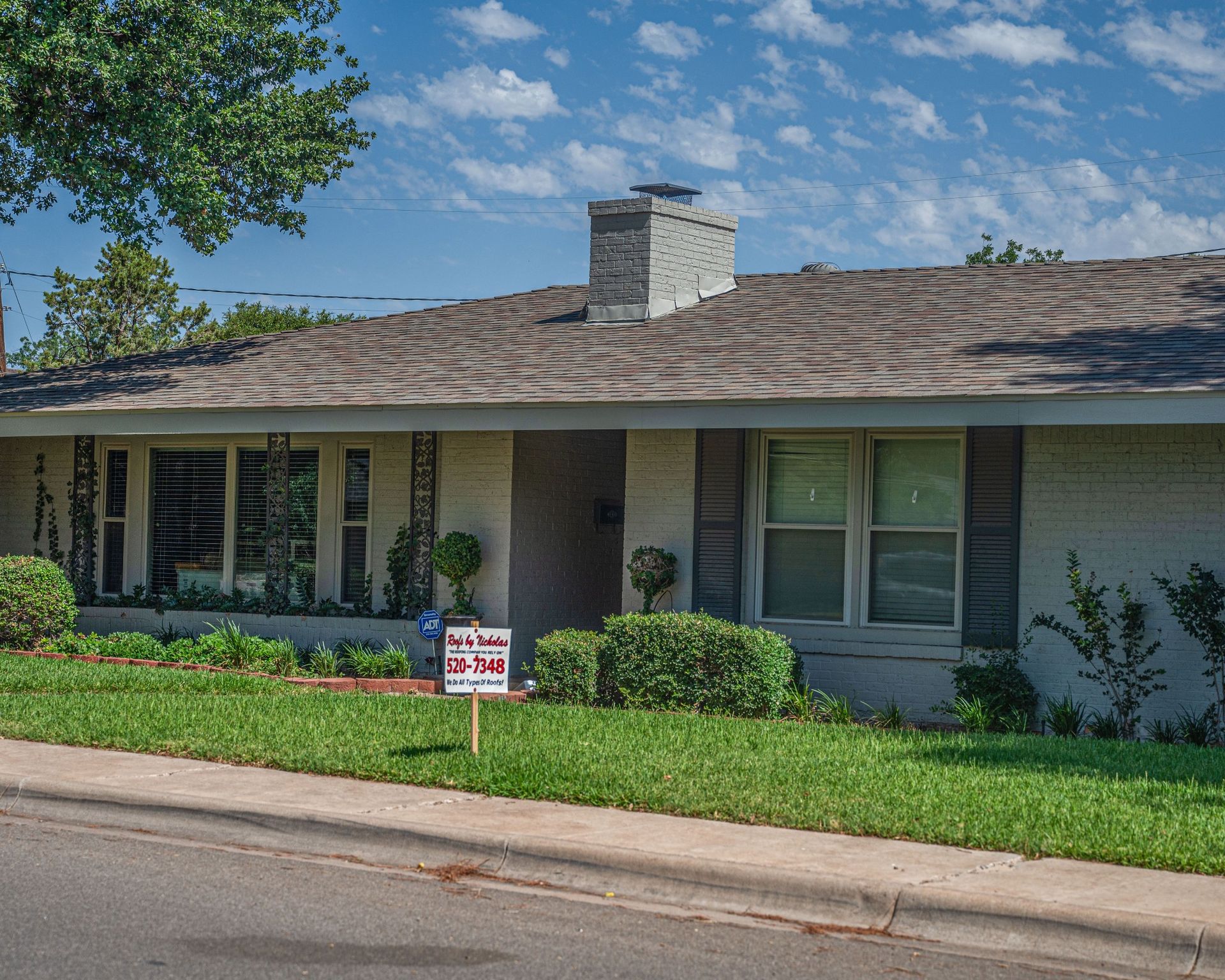 Single-story house with new roof installation and Roofs by Nicholas yard sign in front