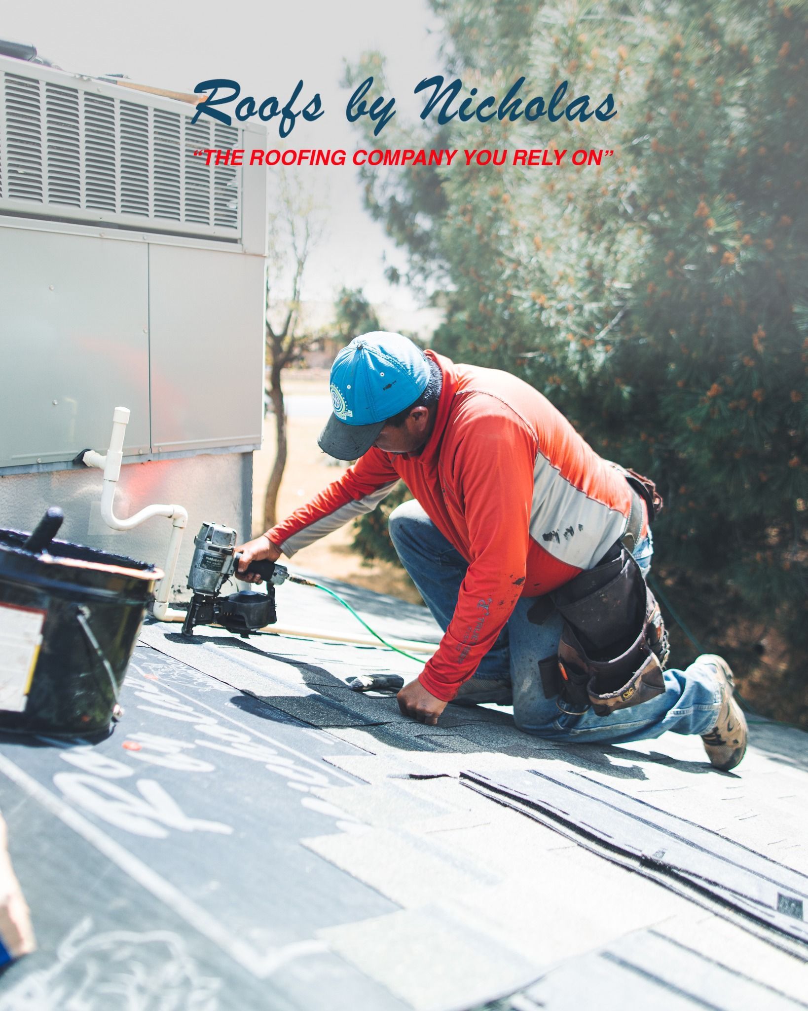 Roofer in red shirt and blue cap installing shingles on roof with nail gun near HVAC vent