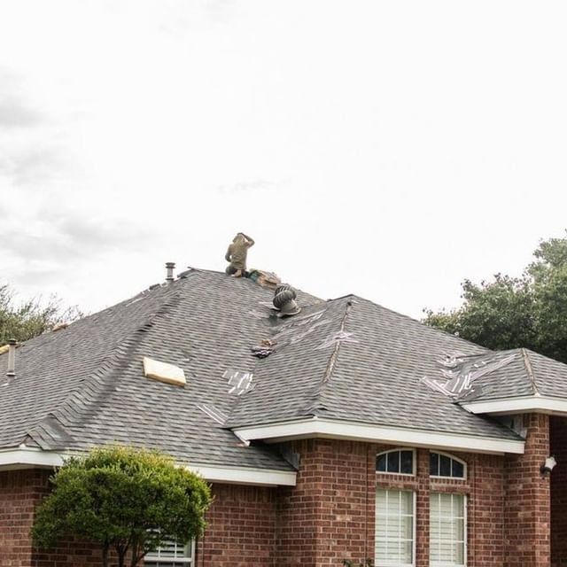 Roofer repairing storm damaged asphalt shingle roof on brick home