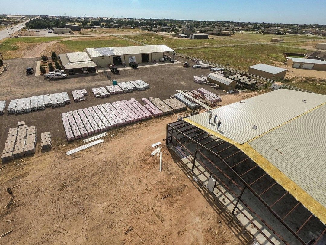 Aerial view of Roofs by Nicholas facility yard with stacked roofing materials and metal building under construction