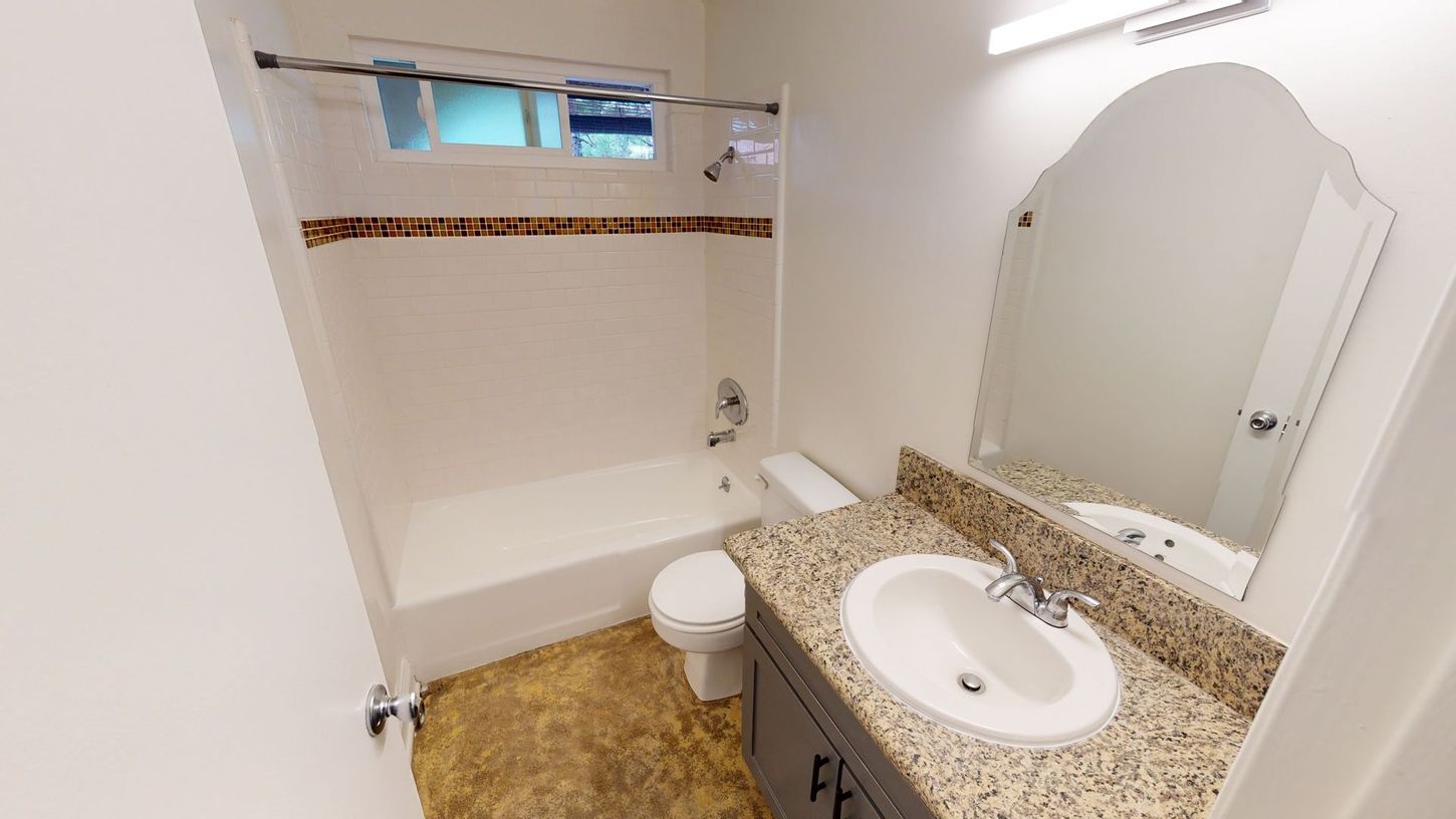 Bathroom with a bathtub, toilet, sink, and mirror. White walls with brown accent tiles.