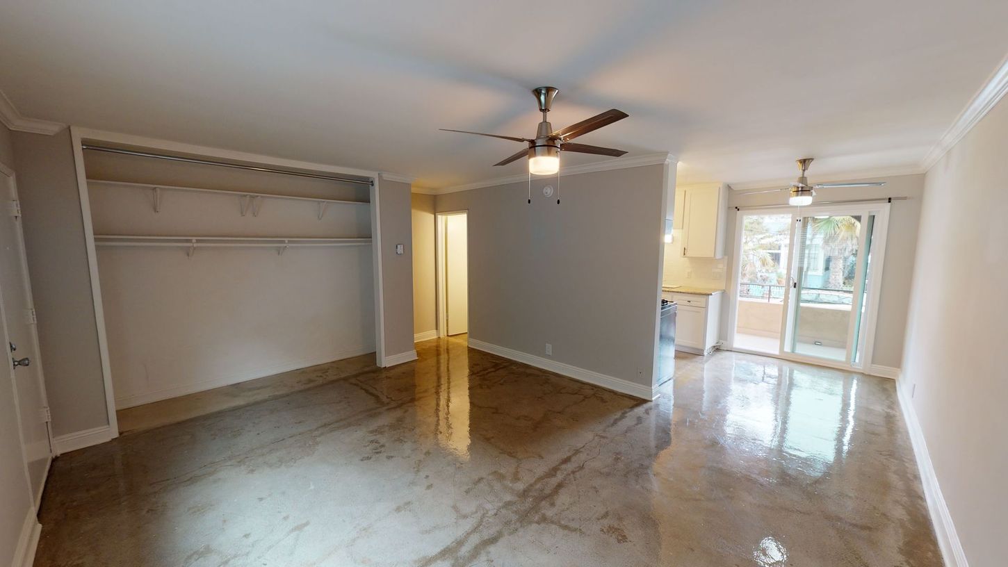 Empty apartment interior with polished concrete floor, closet, kitchen area, and sliding glass door.