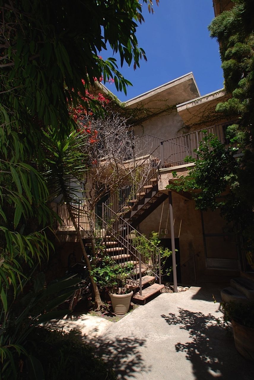 Outdoor staircase to a building with lush foliage, blue sky visible.