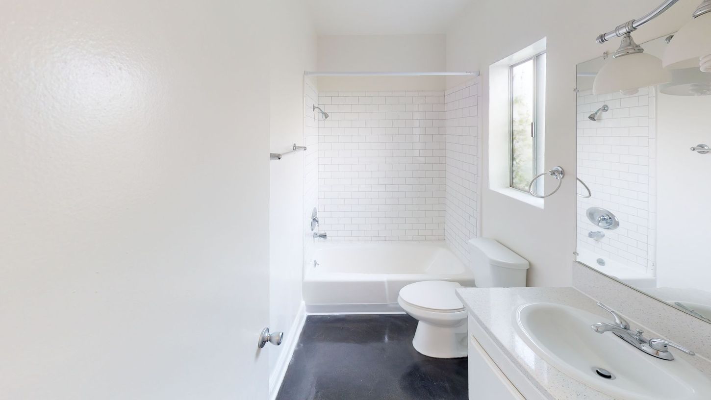 White bathroom with a tub, toilet, sink, and window. Black floor.