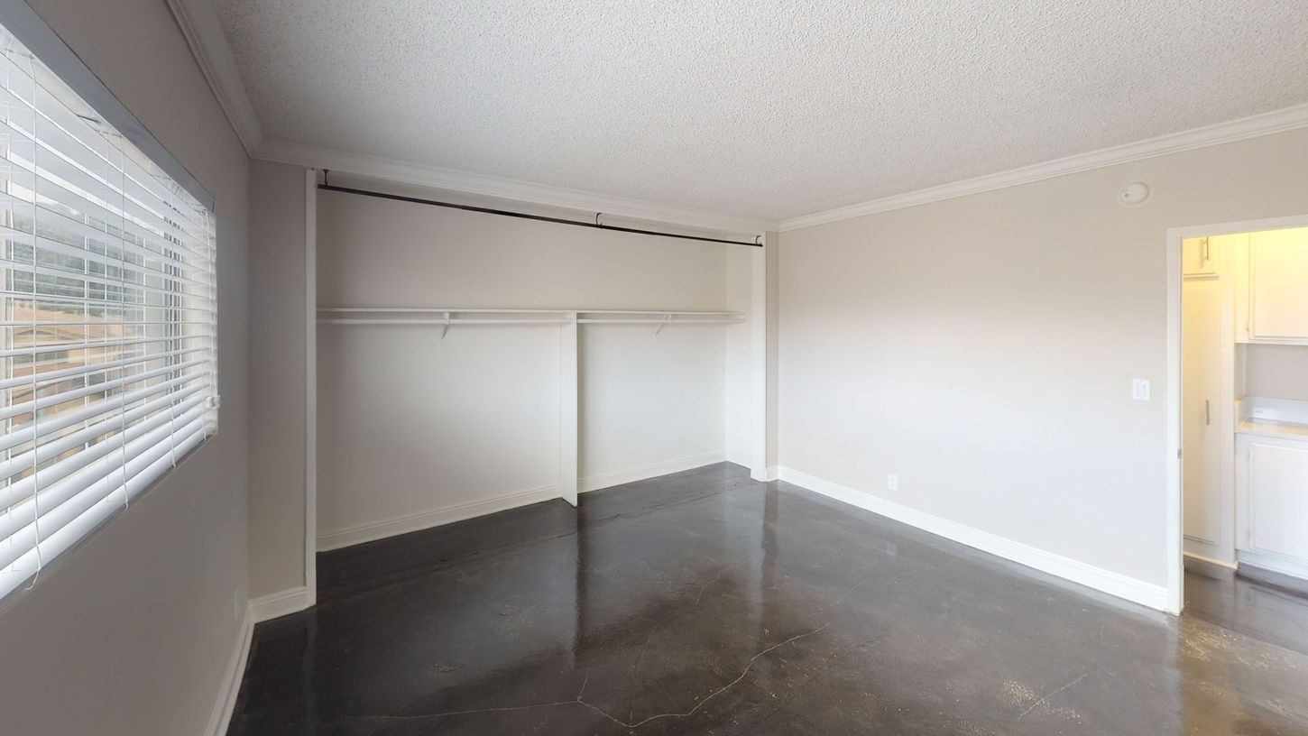 Empty room with a large closet, window with blinds, and a dark floor. Light-colored walls and ceiling.