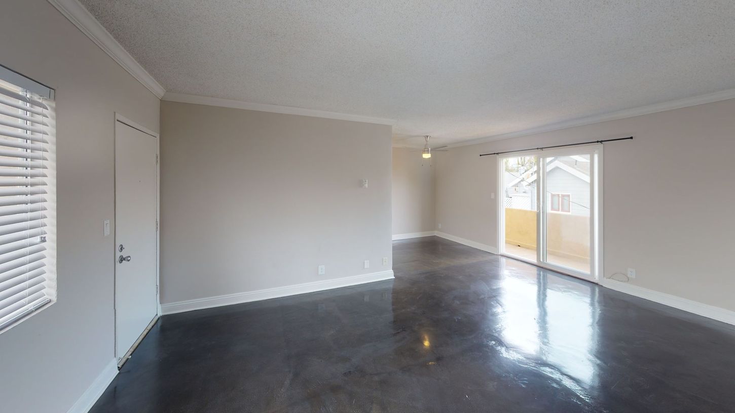 Empty room with dark gray floor, pale walls, and sliding glass door to a balcony.