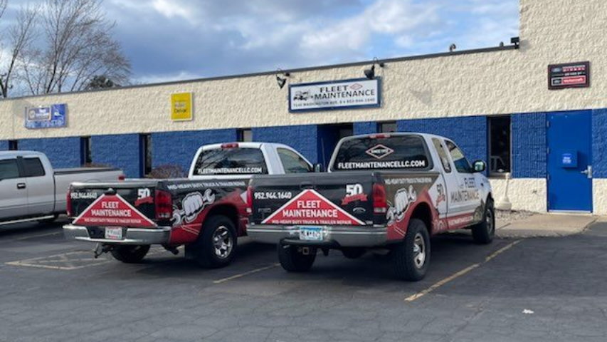 Two white pickup trucks with company logos parked in front of a building with a sign that reads, 