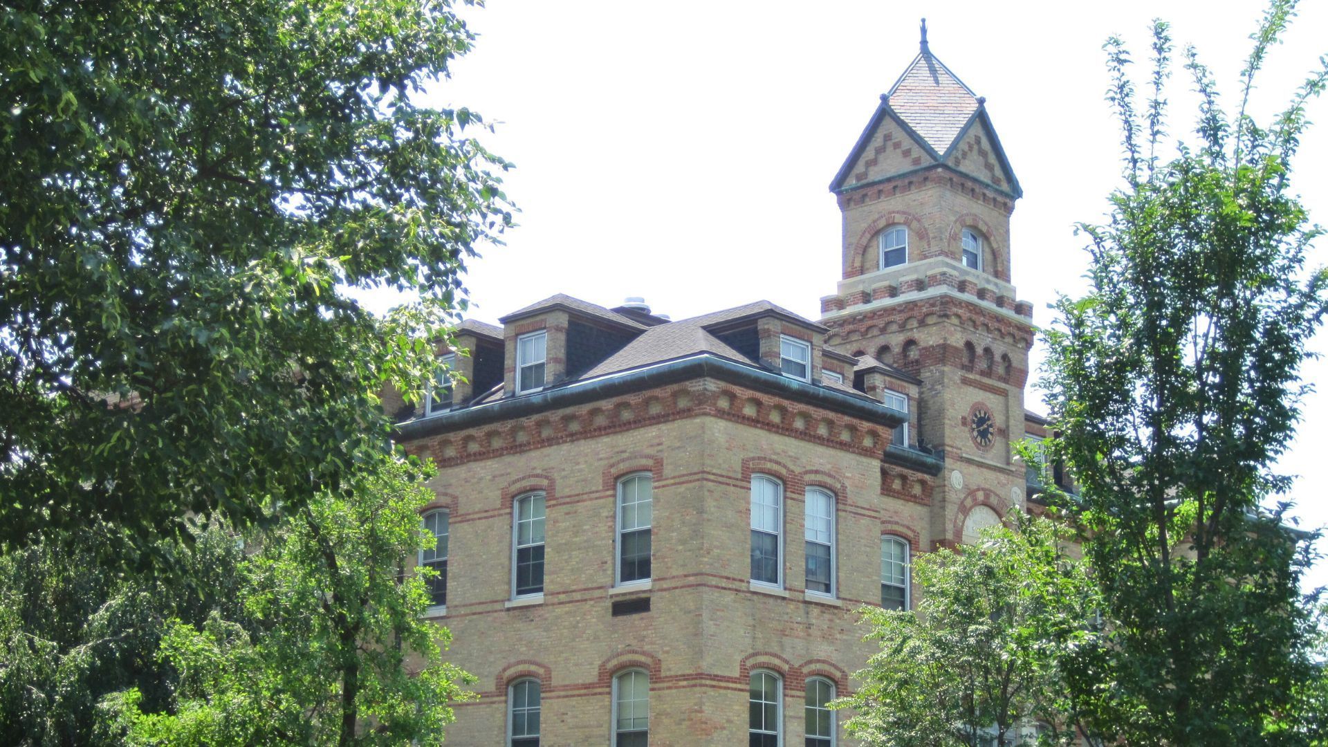 Brick building with tower, framed by trees against a bright sky.