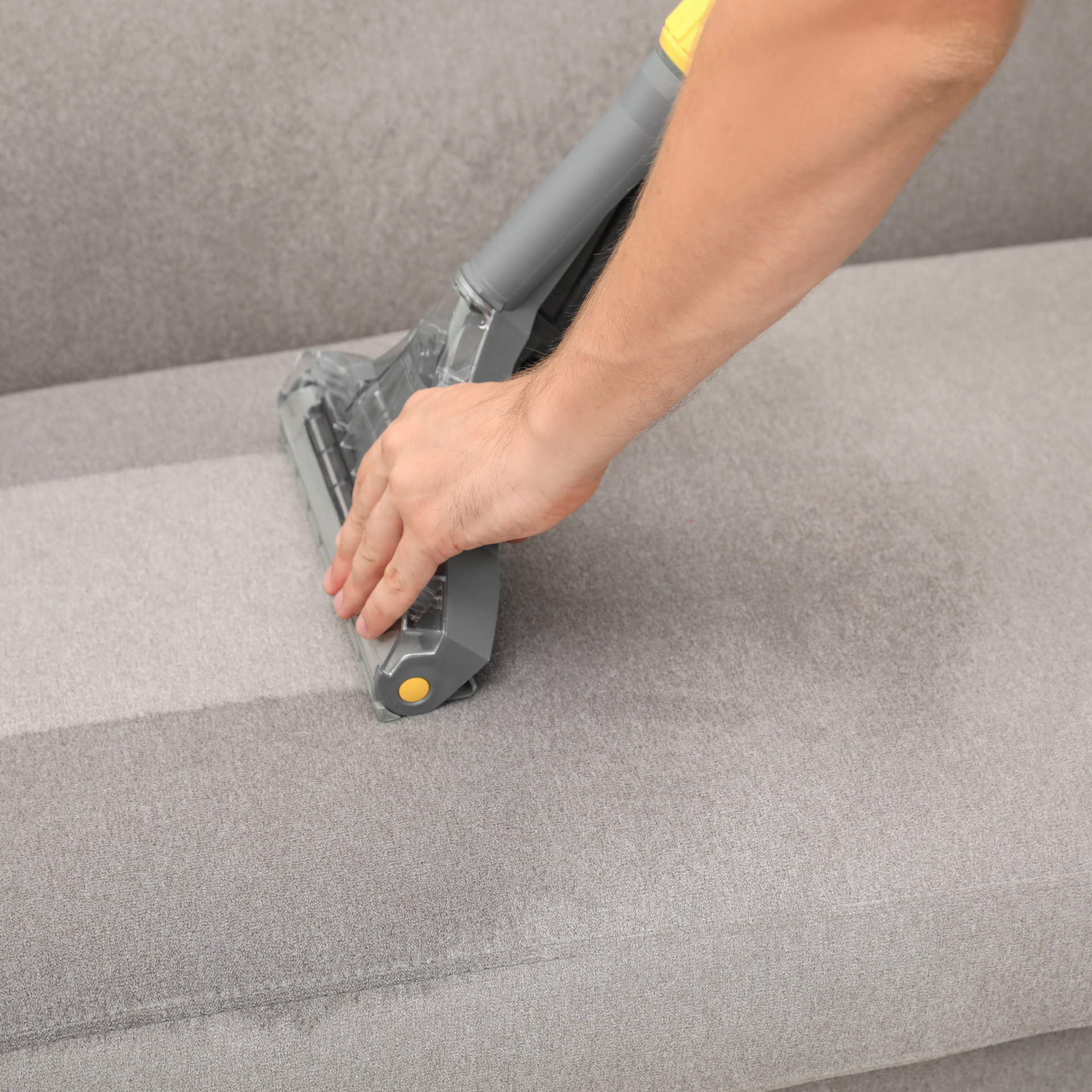 Eco Friend Carpet Clean - Person vacuuming a gray sofa, showing the cleaned area.