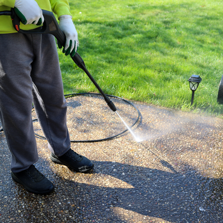 Eco Friend Carpet Clean - Person in gloves pressure-washing a dark sidewalk in front of green grass and a small light.