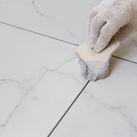 Eco Friend Carpet Clean - Gloved hand using a grout sponge to clean grout on white marble-like tile floor.
