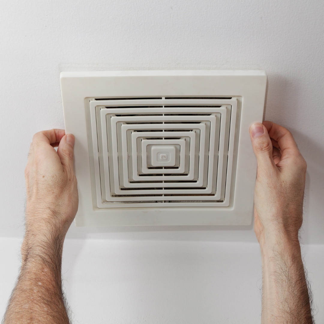 A person is holding a square vent on the ceiling.