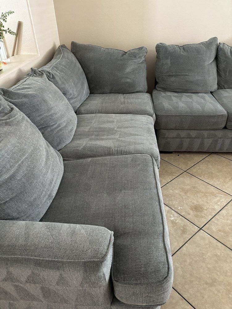 Eco Friend Carpet Clean - Gray sectional sofa in a corner of a room, with textured fabric and several large pillows.