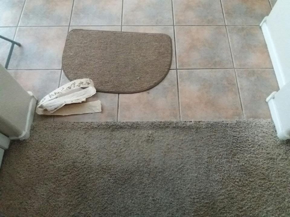 A door mat is sitting on a tiled floor next to a carpet.